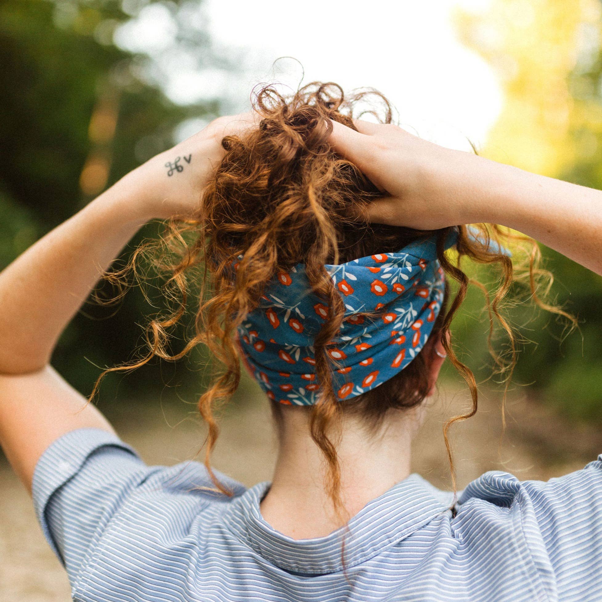 Person with curly hair wearing a blue headscarf with orange patterns, standing outdoors.