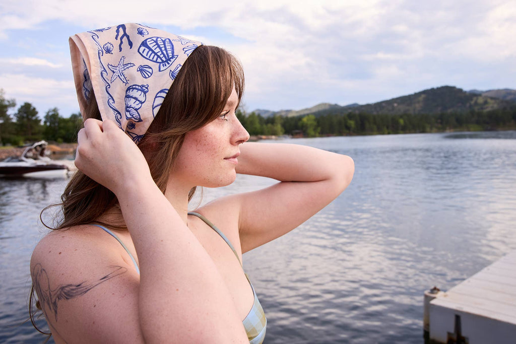 Human with a handkerchief 
on their head by a lake.