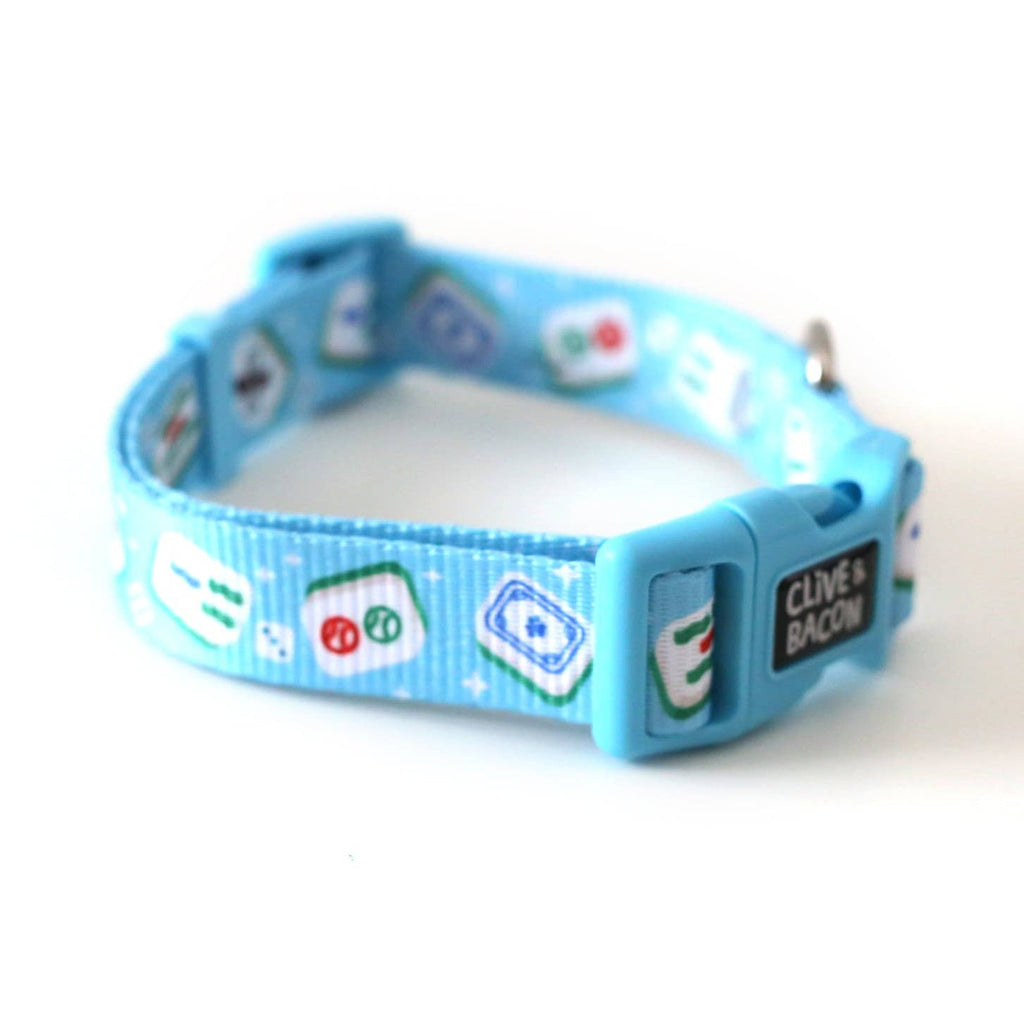 A bright blue pet collar with a pattern of green, white, and red classic mahjong tiles, featuring a bright blue plastic buckle with a black silicone patch that reads 'CLIVE + BACON'.