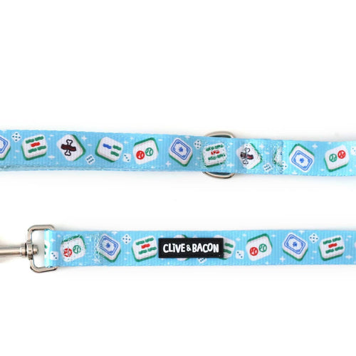 A bright blue dog leash with a repeating pattern of mahjong tiles and dice, featuring a black metal clasp on one end and a black fabric brand label reading 'CLIVE & BACON' on the other.