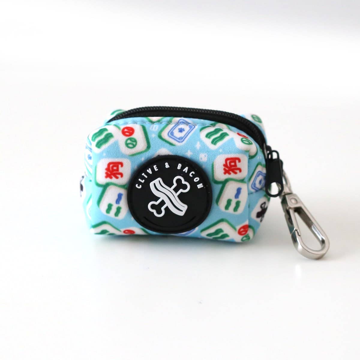 A small zippered pet waste bag with a bright blue background and a classic mahjong tile print. A round black circular patch with the text 'CLIVE & BACON' in white, along with a silver metal carabiner clip.
