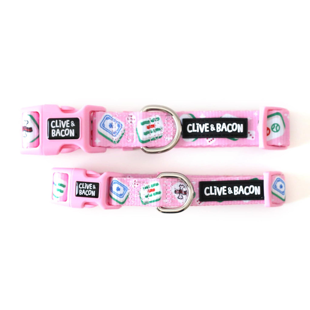 Two bright pink pet collars with silver metal hardware, featuring a repeating pattern of classic mahjong tiles and a black silicone patch that reads 'CLIVE & BACON' in white letters.
