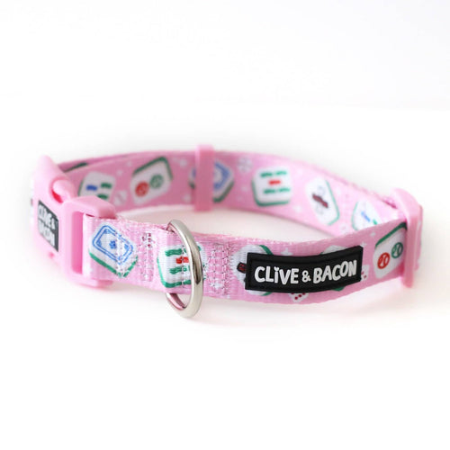 A pink pet collar with a silver metal ring and a black patch that reads 'CLIVE & BACON' in white text. The collar is decorated with a pattern of green, blue, and red mahjong tiles on a shiny polyester webbing in a bright pink.