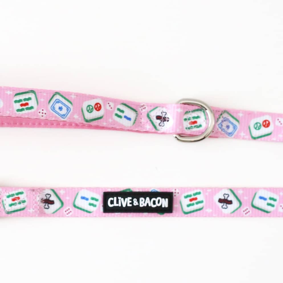 A pink pet collar with a repeating pattern of mahjong tiles and a black fabric brand label reading 'CLIVE & BACON'.