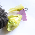 A small black dog is partially visible on the left, interacting with a bright yellow-green plastic bag tied to a pink cloud-shaped bag holder. The holder has the text 'CLIVE & BACON' printed on it, indicating the brand.