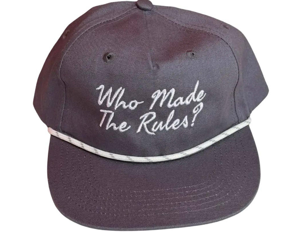 A vintage navybaseball cap with white embroidered text reading 'Who Made The Rules?' on the front, featuring a white patterned trim across the brim, set against a plain white background.